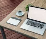 A minimalist outdoor workstation with laptop, coffee, and tablet on a rustic table.